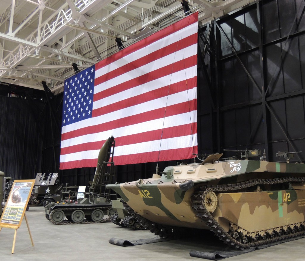 large American flag behind military vehicles on display