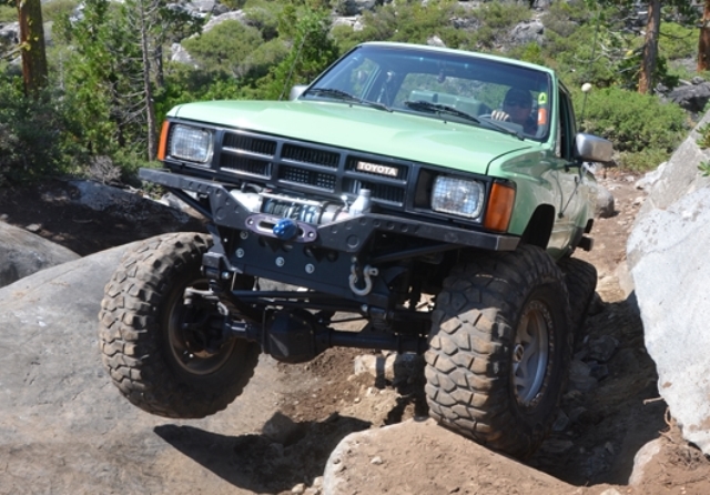 an off road modified toyota tacoma crawling up rocks on a trail