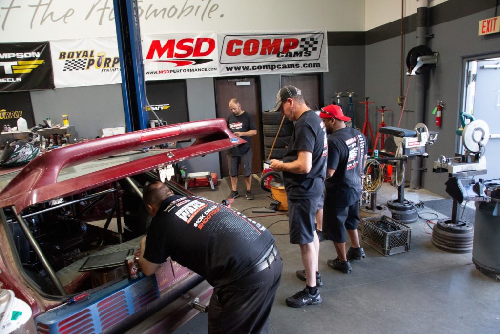 men working on a fox body mustang drag car in a shop