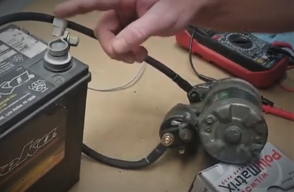 man using a battery to test an enigne starter on a work bench
