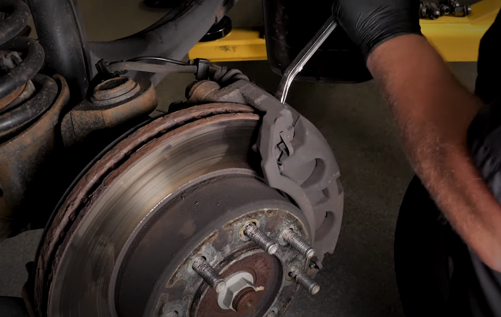 man removing a rusty brake caliper from a rotor bracket