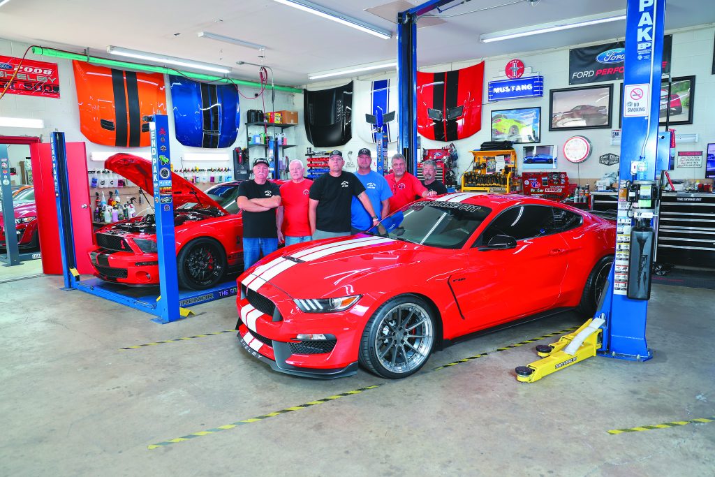 men standing in a shop with late model mustangs