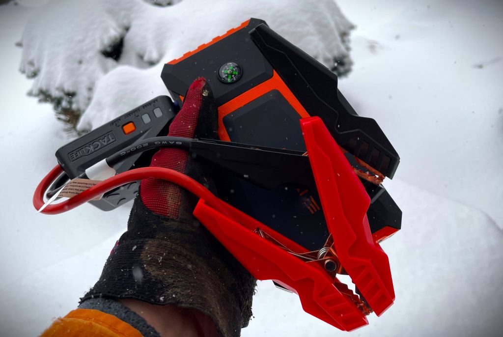 man holding a battery jump starter pack in the snow