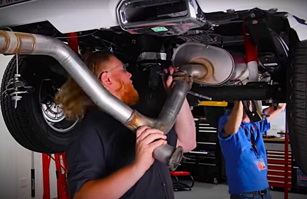 two men removing an exhaust system on a truck